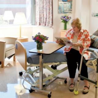 A patient sitting in a hospital room, reading next to a bed with a bouquet of flowers on the table.