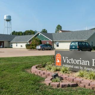 A view of the Victorian Inn with a parking area, cars, and a visible water tower in the background.