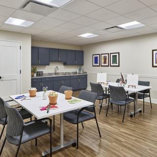 A well-organized meeting room with tables and chairs, featuring a kitchenette and decorative artwork.