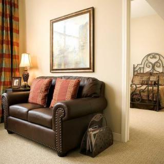 A cozy living room with a leather sofa and cushions, adjacent to a bedroom.