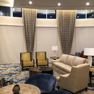 A modern living room features elegant furnishings including a sofa, armchairs, and a round coffee table, complemented by tall curtains and a patterned carpet.