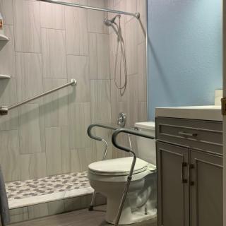 A modern, accessible bathroom featuring a shower with grab bars and a toilet with handrails.