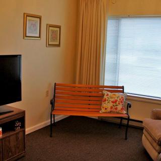A cozy living room with a wooden bench, television, and large window with curtains.