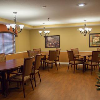 A neatly arranged dining room with several tables and chairs, decorated with chandeliers and artwork on the walls.