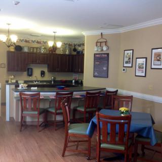 A cozy dining area with a kitchen bar, wooden chairs, and framed artwork on the walls.