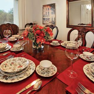 A formal dining table set with patterned dinnerware, red napkins, and a central floral arrangement.