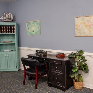 A neatly organized office space with a desk, chair, and shelving unit adorned with books and decorative items.