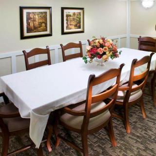 A dining room setup with a white tablecloth-covered table, surrounded by wooden chairs, and a floral centerpiece.
