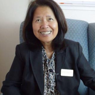 A woman in business attire smiles while sitting indoors.