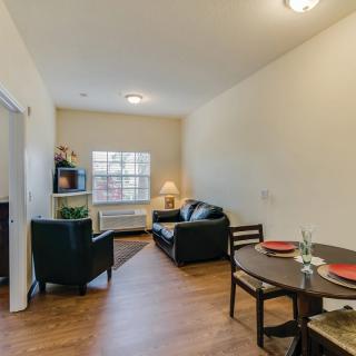 A cozy apartment living room with a dining area, featuring a sofa, chairs, and a table under soft lighting.