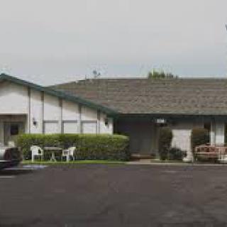 A small motel with a parking area and outdoor chairs.