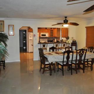 An open dining area seamlessly connected to a modern kitchen, featuring a large dining table with chairs and a ceiling fan above.