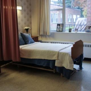 A hospital room with a bed next to a window, featuring curtains and a lamp.