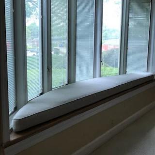 A cozy window seat with a cushion, framed by large windows and blinds, offering ample natural light.
