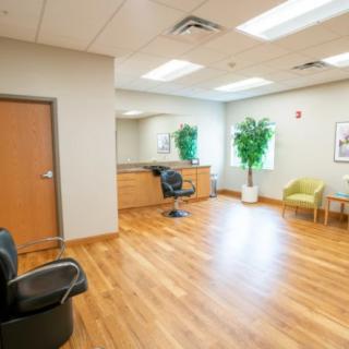 A spacious office waiting area with wooden flooring, several chairs, and a large potted plant.