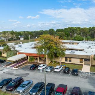 Aerial view of a school building surrounded by a parking lot and greenery under a clear blue sky.