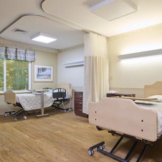 A bright and clean hospital patient room featuring two adjustable beds and natural light from a nearby window.