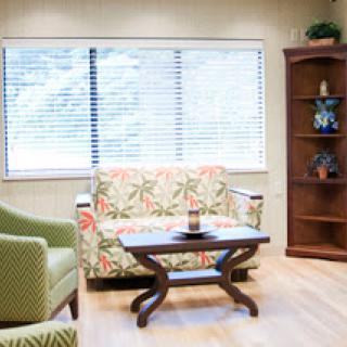 A cozy living room setup featuring a colorful floral sofa, a green armchair, and a wooden table by the window.