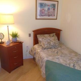A cozy bedroom with a single bed, nightstand, and warm lighting.