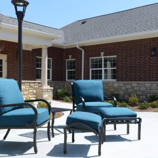 A patio featuring blue cushioned chairs in front of a brick building on a sunny day.