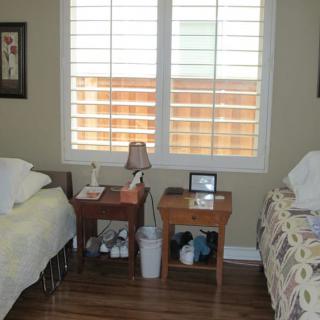 A cozy bedroom with twin beds, a central nightstand, and a window adorned with wooden blinds.