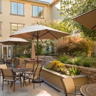 A cozy outdoor patio with seating arrangements and umbrellas, surrounded by a lush garden.