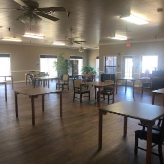 A spacious common area featuring neatly arranged tables and chairs, illuminated by natural light.
