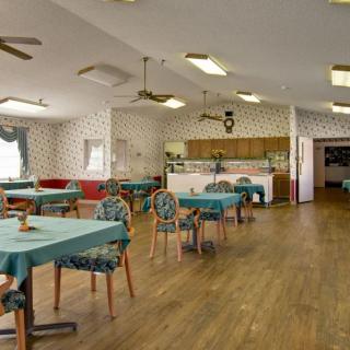 A spacious dining room with multiple tables and chairs, featuring wooden flooring and ceiling fans.
