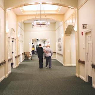 Two individuals stroll down a brightly lit hallway, highlighting the warmth of companionship in an inviting indoor space.