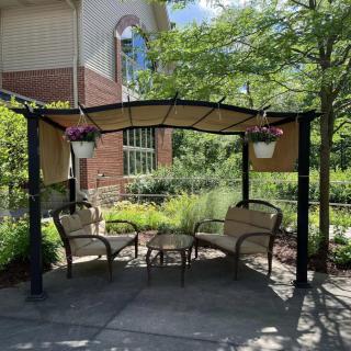 A cozy outdoor gazebo with chairs and a table, surrounded by greenery and hanging plants.