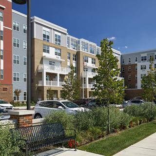 A modern apartment complex in an urban residential area with well-maintained landscaping and parked cars.