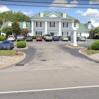 A view of a hotel with a spacious parking lot surrounded by greenery.