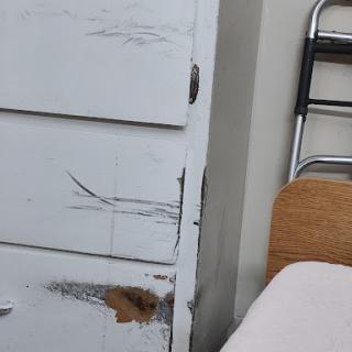 A close-up view of a damaged white wooden cabinet with visible scratches and wear.
