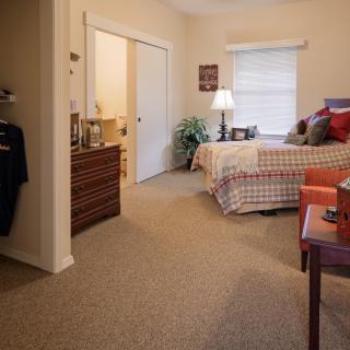 A cozy bedroom with a neatly arranged bed, dresser, and warm lighting.