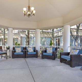 A spacious outdoor patio with wicker furniture and cushioned seating under a gazebo, featuring a chandelier and surrounded by columns.