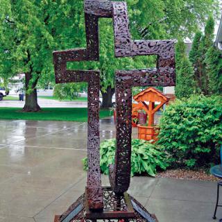 A striking metallic cross sculpture set in a serene garden.
