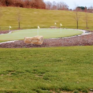 A serene putting green surrounded by grass and gentle hills.