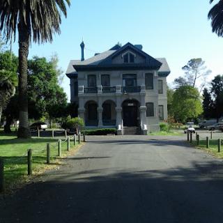 A picturesque historical mansion surrounded by lush greenery and palm trees.
