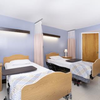 A view of a hospital patient room featuring two beds with bedside tables and curtains for privacy.