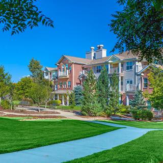 A beautiful residential building surrounded by lush greenery and a well-maintained lawn under a clear blue sky.