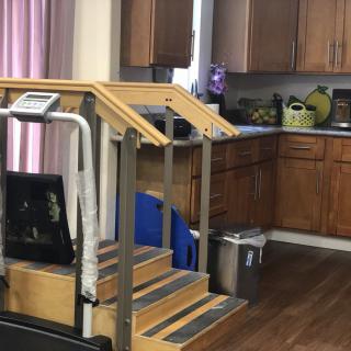 Indoor physical therapy setup with training stairs next to a kitchen area.