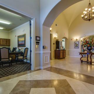 A luxurious interior with a grand foyer, featuring a chandelier, marble flooring, and an adjoining office space.