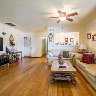 A cozy living room with wooden floors, featuring comfortable sofas, a coffee table, a ceiling fan, and a television.