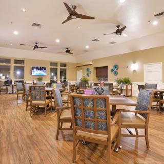 A spacious indoor dining area with wooden floors, neatly arranged tables and chairs, and ceiling fans.
