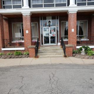 Entrance of a brick building with steps leading up to the door, flanked by windows and greenery.