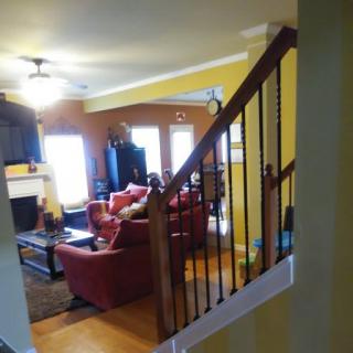 A cozy living room with a staircase view, featuring sofas, a television, and a fireplace.