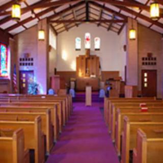Interior view of a church with pews leading to an altar, featuring stained glass and wooden architecture.