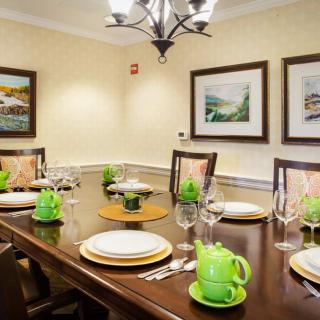 A neatly set dining table with green teapots and decorative plates in a warmly lit room featuring artwork on the walls.