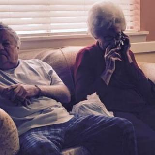 An elderly couple sitting and relaxing on a couch in their home.