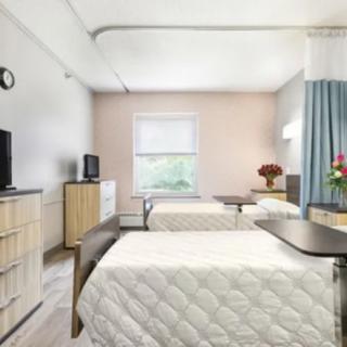 A hospital room with two beds, televisions, and a window with curtains.